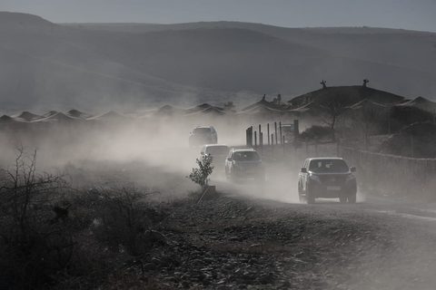 Geländewagen wirbeln Staub auf einer Piste vor Wüstenzelten auf