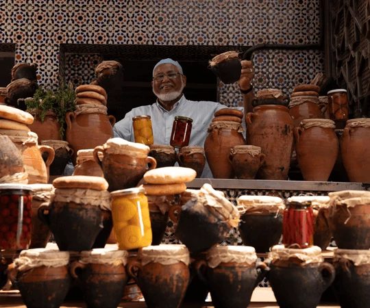 Glimlachende verkoper achter terracotta kruiken en ingemaakte producten op een marktkraam in Marokko