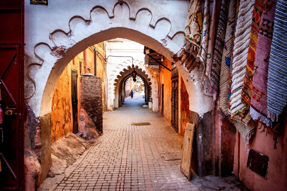 Steeg in de medina van Marrakech met witte bogen en hangende tapijten